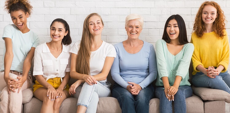 Smiling Diverse Women Sitting On Sofa Over White Brick Wall